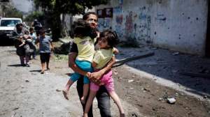 A Palestinian man carries children in the Shejaia neighbourhood, which was heavily shelled by Israel during fighting, in Gaza City